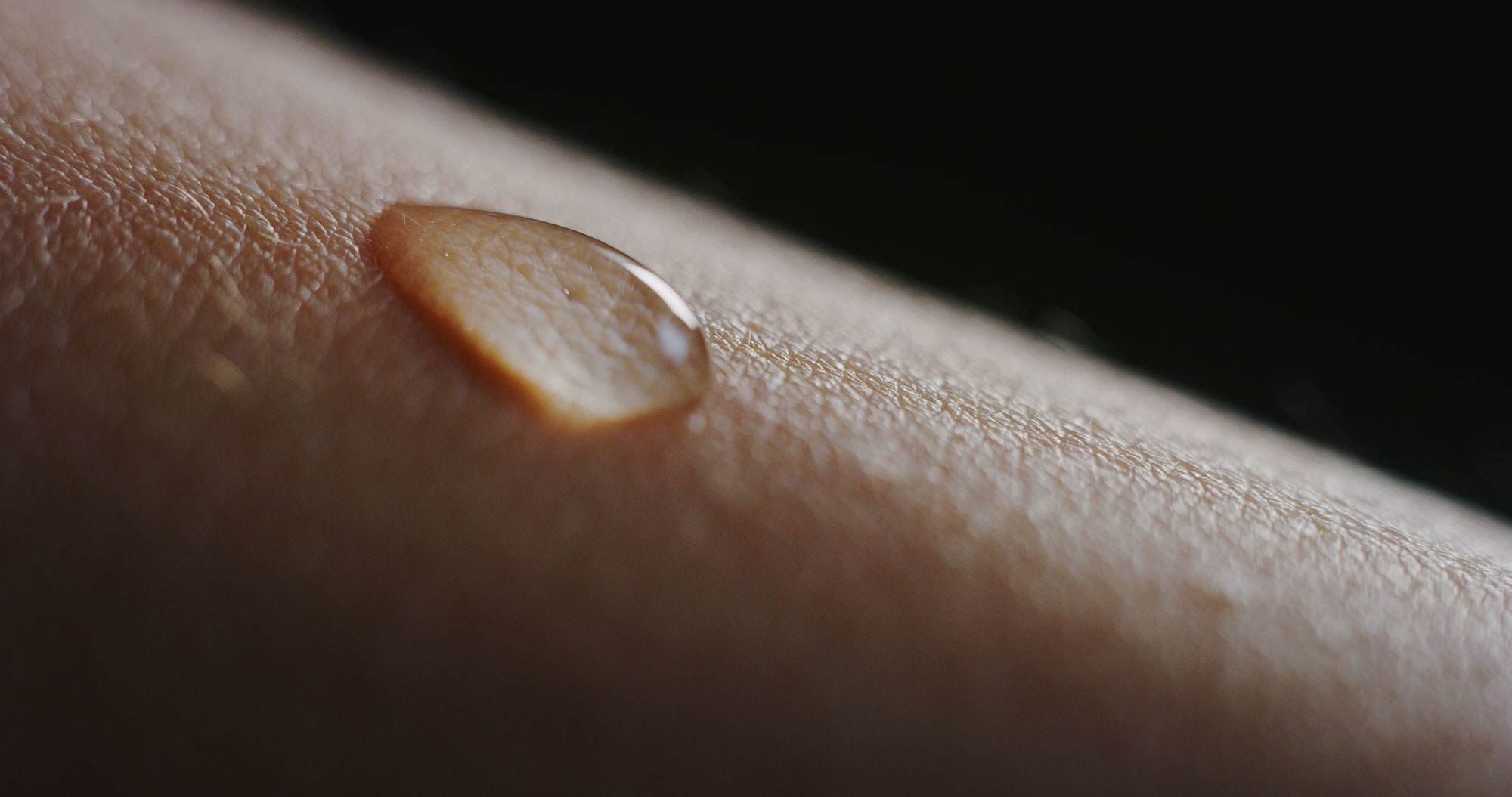 Close up of a drop of fluid on someone's skin. The skin is white with hairs standing up.
